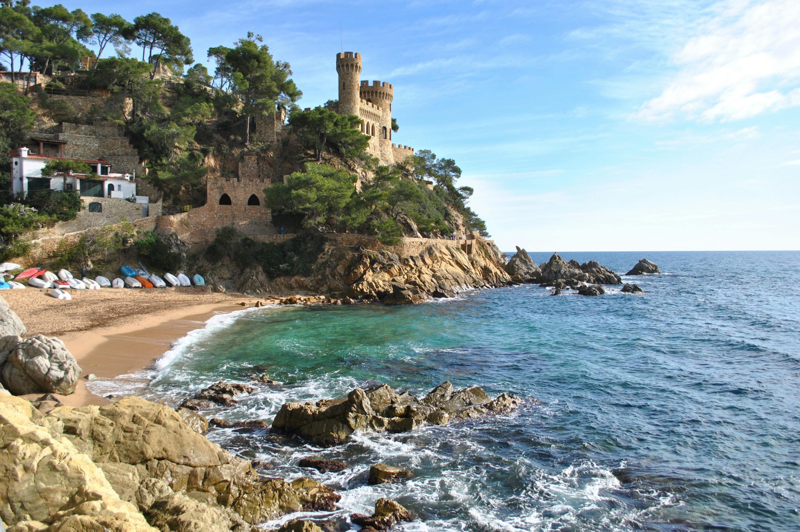 Picturesque medieval castle on rocky cliffs overlooking a vibrant blue sea with sandy beach.